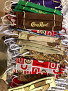Stack of handmade fabric face masks with various patterns, including camouflage and sports logos, on a workbench.