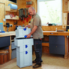 Woodworker stacking modular plastic storage boxes in a workshop with hand tools on pegboard wall