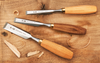 Three Western-style woodworking chisels with wooden handles on a wood surface with wood shavings.