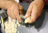 Hands using a carving knife to whittle a small wood piece with shavings on a table