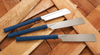 Three Japanese saws with new blue TPE handles resting on various wood pieces in a workshop setting.