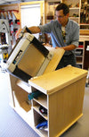 Woodworker installing a Delta planer into a custom plywood cabinet with storage shelves in a workshop