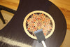 Close-up of a wood finishing brush applying finish to a dark wood surface with a decorative marquetry inlay.