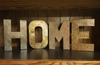 Wooden block letters spelling HOME with textured faux finish on a wood shelf