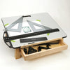 Adjustable drafting table with glass top, wooden base, and drawer holding woodworking squares and rulers