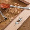 Wood chisel and Forstner bit near a mortised keyhole plate in hardwood with wood shavings