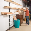 Man organizing long lumber on adjustable metal wall-mounted shelving in workshop space