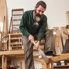 Woodworker using a Japanese pull saw to cut a wooden board in a workshop.