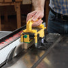 Hand using a yellow push block to safely guide wood through a table saw blade.