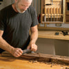 Woodworker sharpening a cabinet scraper on a wooden workbench with chisels in background