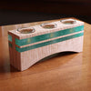Curved maple wood tealight holder with turquoise resin inlays and three glass cups on wooden table