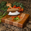 Striped hardwood chopping block with curved ulu knife and chopped vegetables on granite countertop